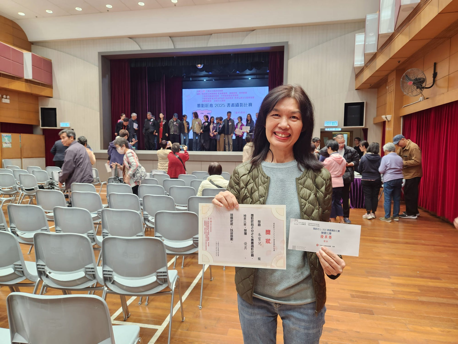 Woman holding certificates in a conference room with attendees in the background